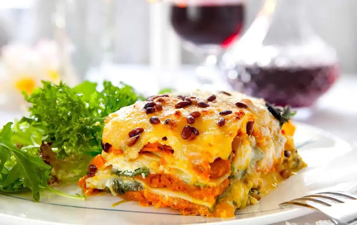 Plato de pasta gratinada con queso y piñones, acompañado de hojas verdes